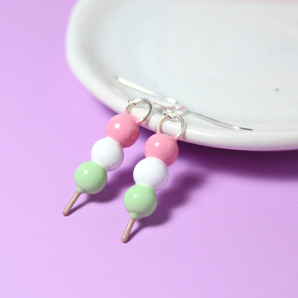 A pair of hanami dango earrings rest against a white jewelry dish.
