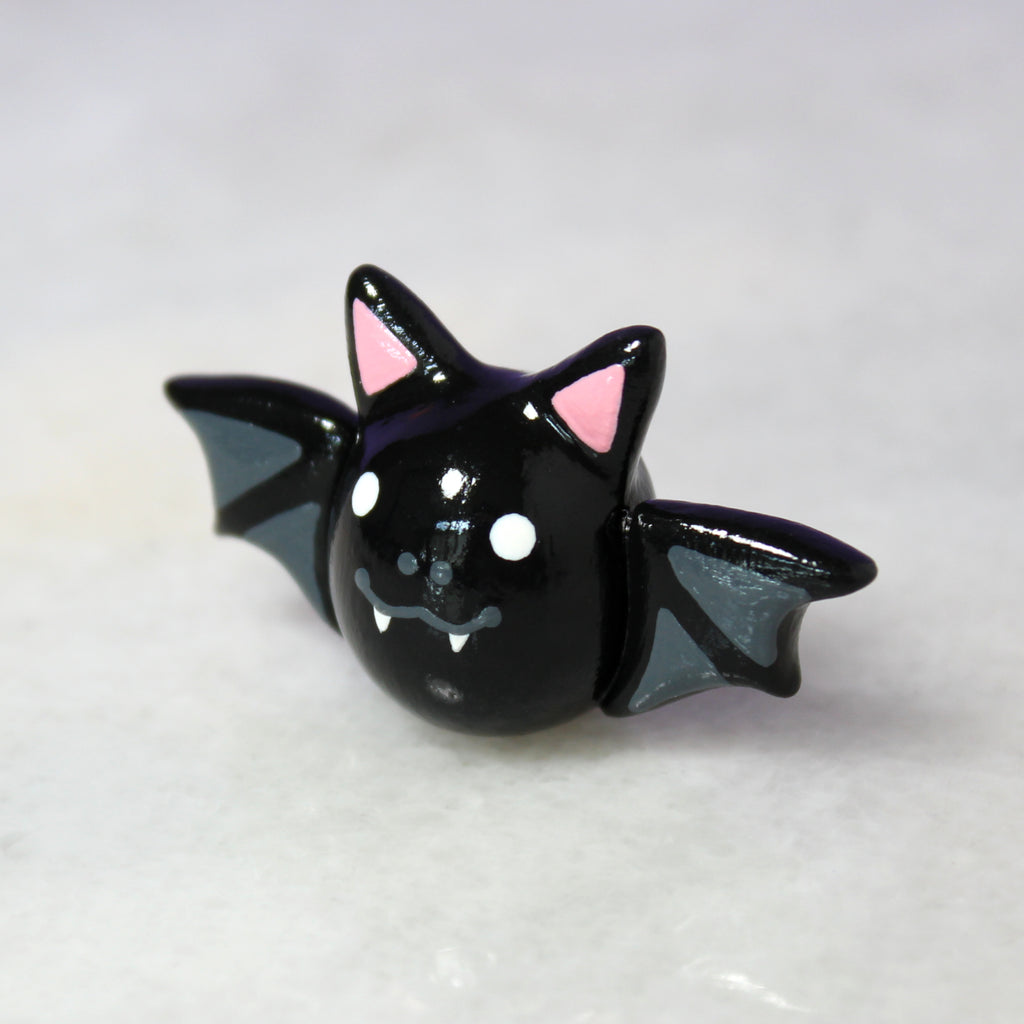 A small black bat figurine sitting on a shiny white surface.