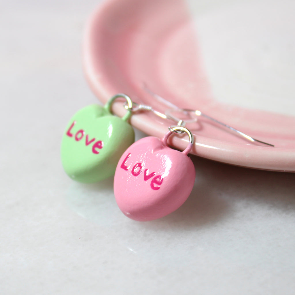 A pair of mismatched candy heart charms hang from sterling silver ear wires.