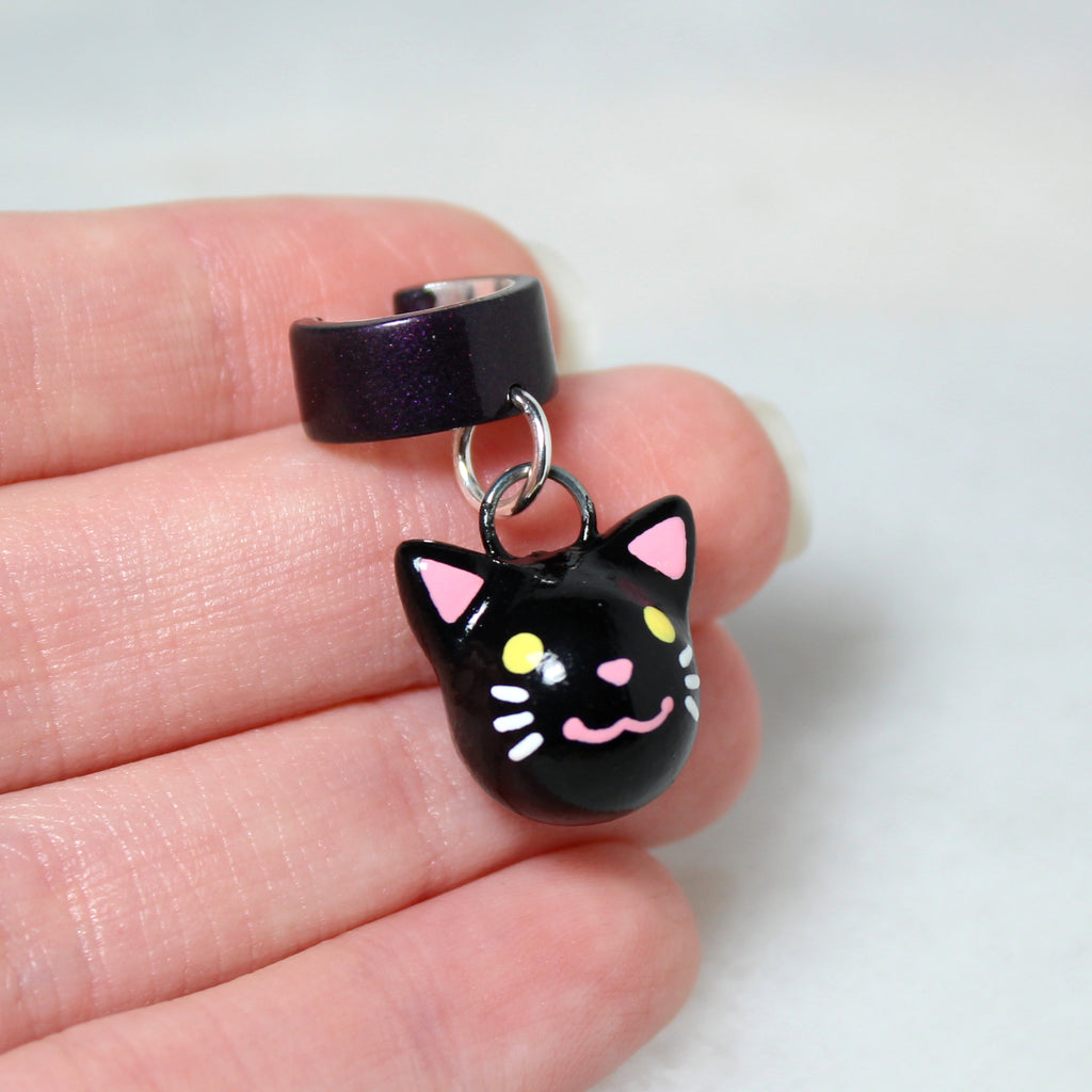 A hand holding a black cat ear cuff. The cat charm is about 3/4 of an inch tall.