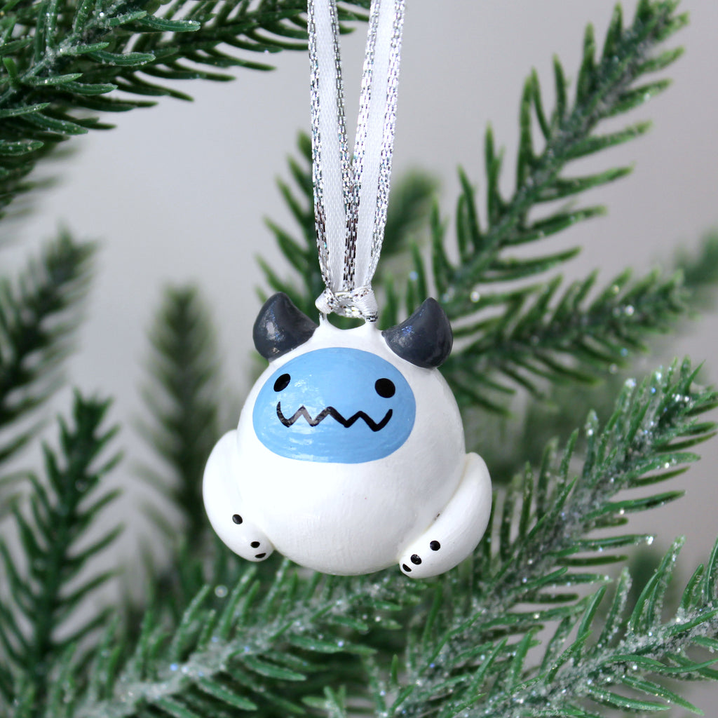 A chubby yeti ornament with a blue face hangs from a Christmas tree.