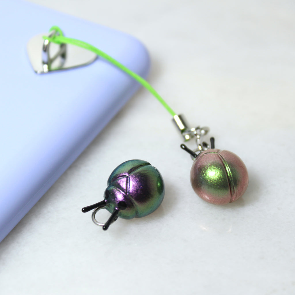 Two iridescent beetle charms sit next to a purple phone case