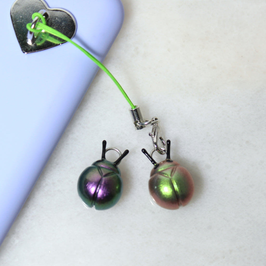 Two iridescent beetle charms sit next to a purple phone case