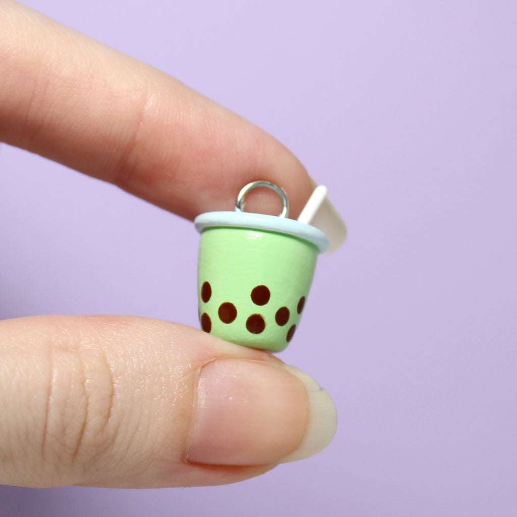 Two fingers holding a bubble tea charm. The charm is 3/4 of an inch tall.