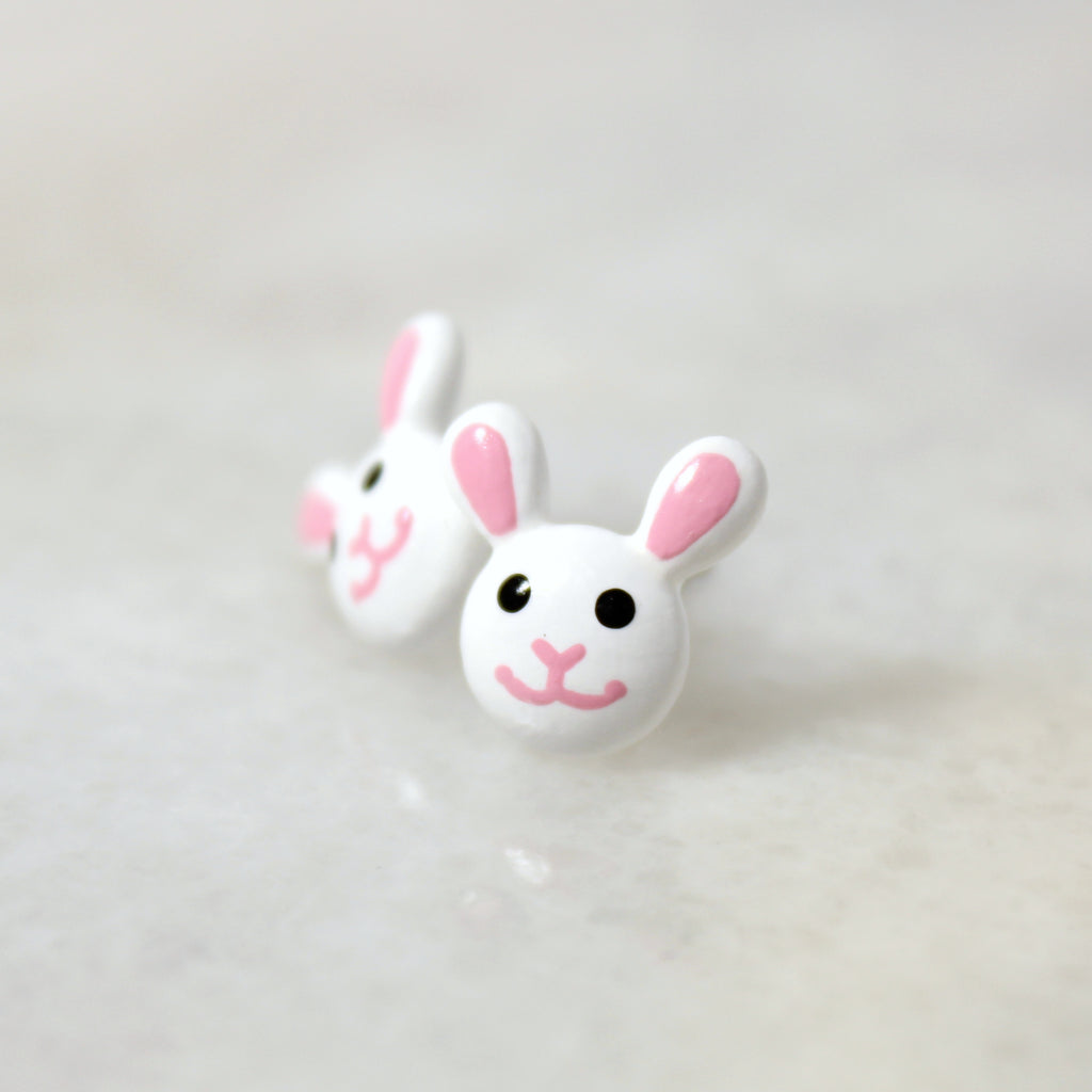 A pair of bunny stud earrings rest on top of a marble surface