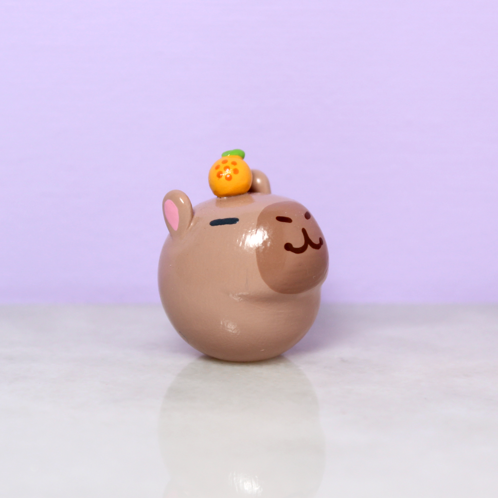 A chubby capybara figurine with a tiny orange on its head.