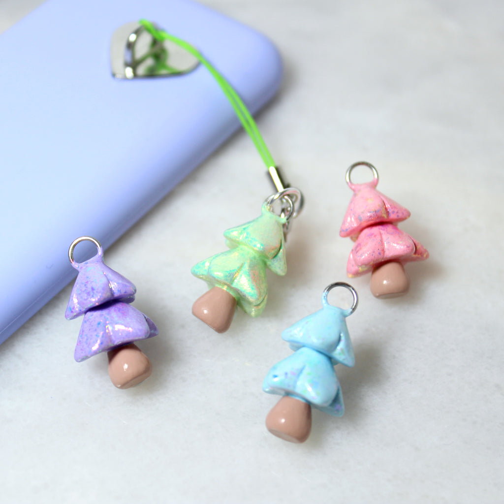 Four sparkly christmas tree phone charms in a variety of pastel colors. A green tree charm is attached to a purple phone case