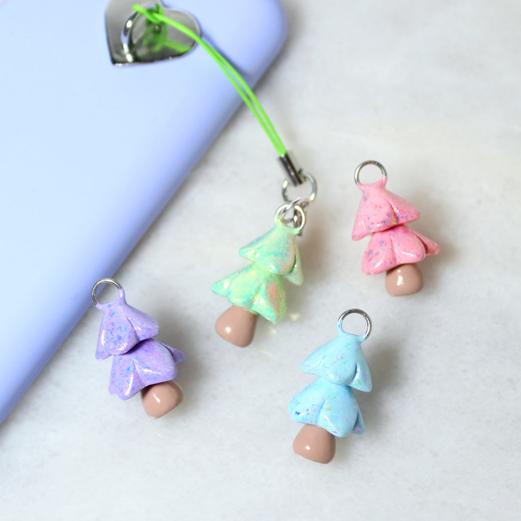 Four sparkly christmas tree phone charms in a variety of pastel colors. A green tree charm is attached to a purple phone case