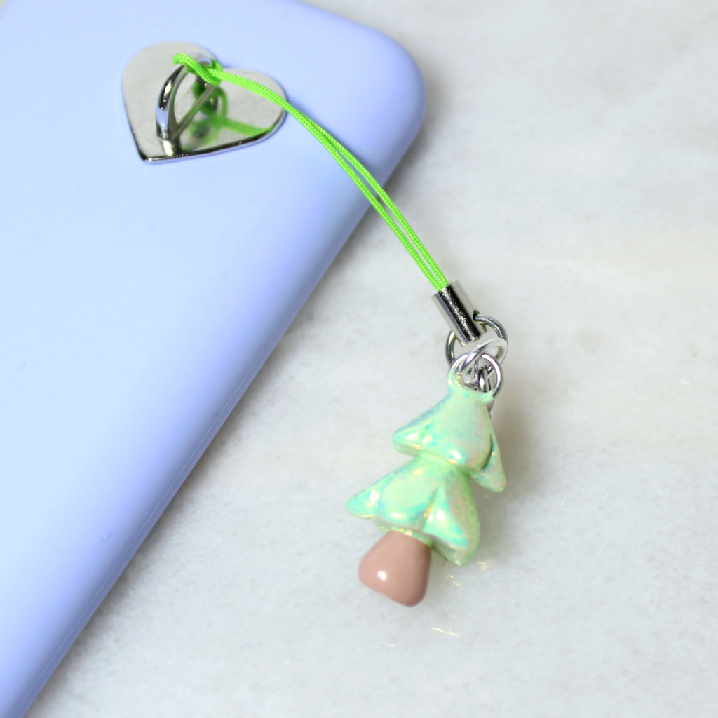 A sparkly pastel green christmas tree phone charm hangs off of a silver phone charm hook. The phone charm hook is attached to a purple phone case