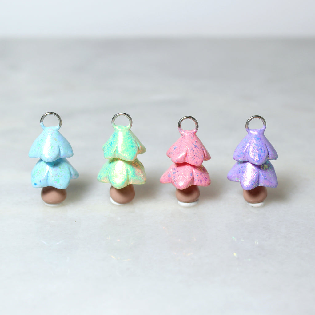 Four sparkly christmas tree charms are lined up in a row. From left to right there is a blue tree, a green tree, a pink tree, and a purple tree