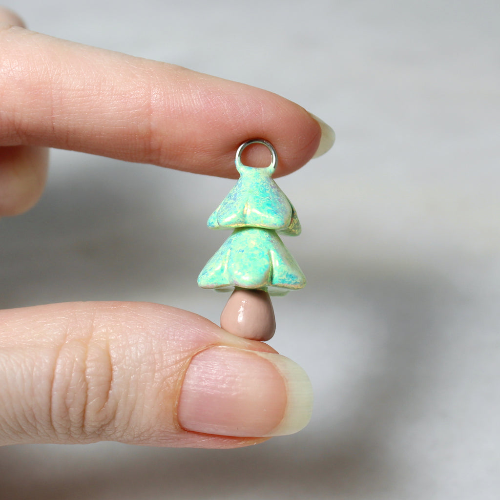 A hand holds a sparkly pastel green christmas tree charm. The charm is about an inch tall