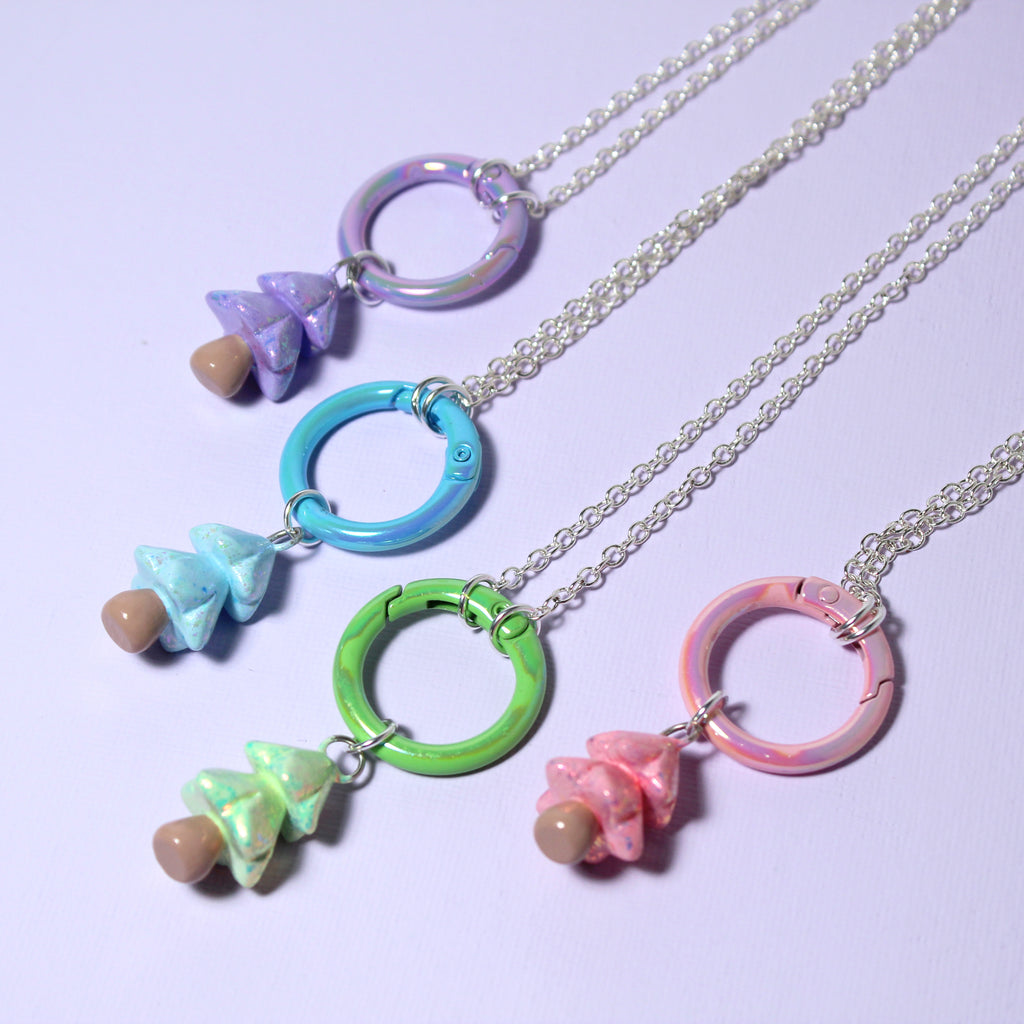Four pastel christmas tree necklaces with large matching carabiner charm keeper clasps rest against a purple surface