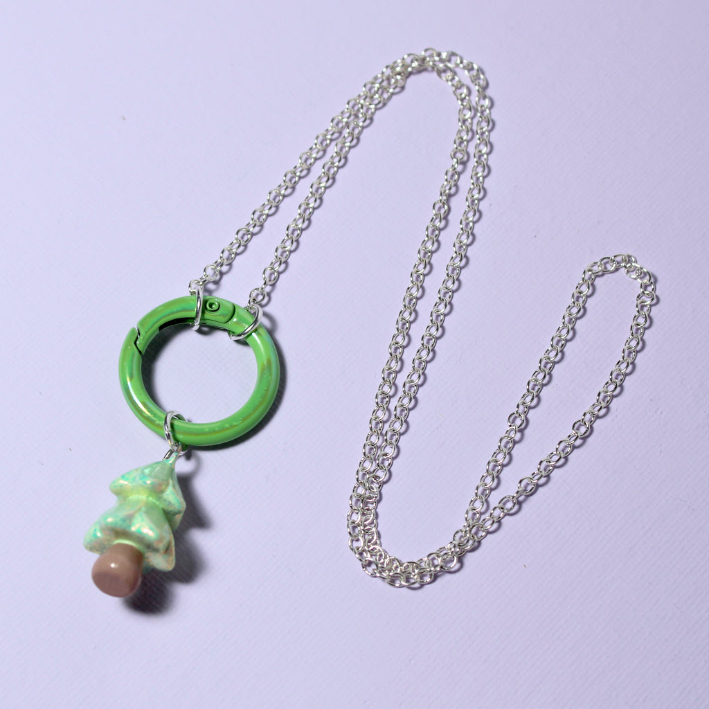 A sparkly green christmas tree charm hangs from a necklace chain with a matching green carabiner clasp. The carabiner doubles as a front clasp to the necklace and a charm holder