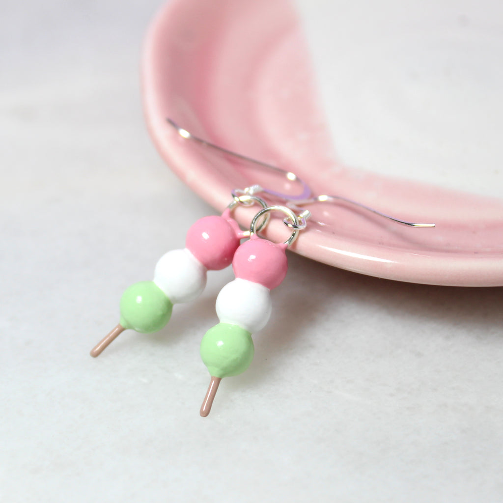 A pair of hanami dango earrings rest against a pink and white jewelry dish.