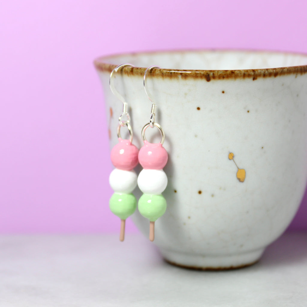 A pair of hanami dango earrings hang from a gray and gold cup.