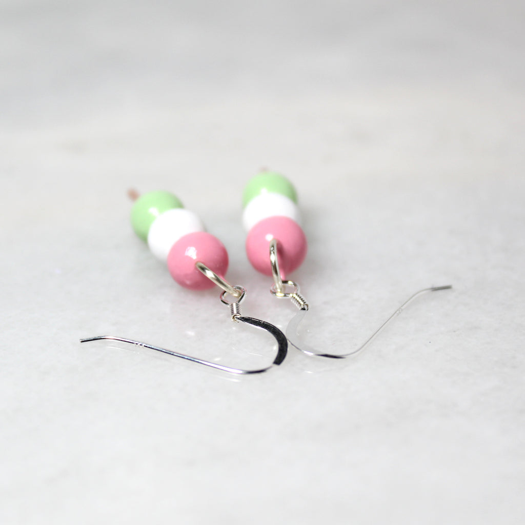 A pair of hanami dango earrings lay on their side with the shiny sterling silver ear wires facing the viewer.