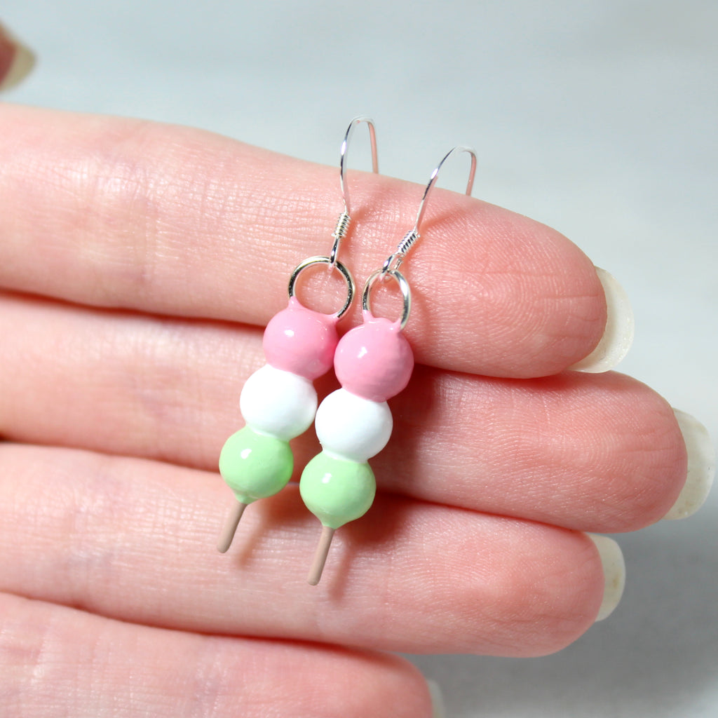 A hand holding a pair of hanami dango earrings. The dango charms are each about one inch long.