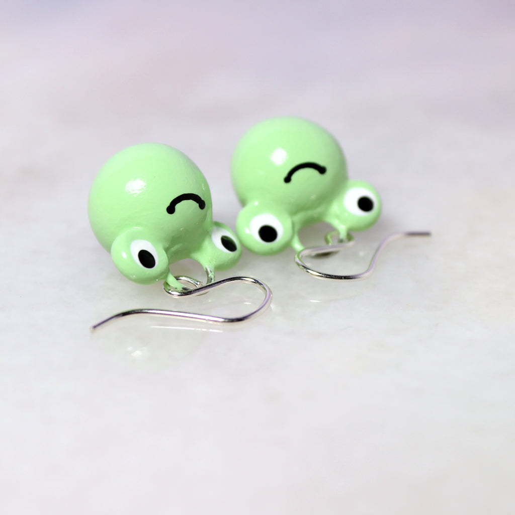 A pair of smiling green frog charms hang from sterling silver earring hooks