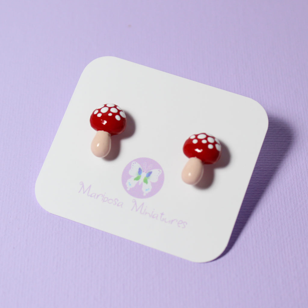 A pair of red mushroom earrings are displayed on a white jewelry backing card