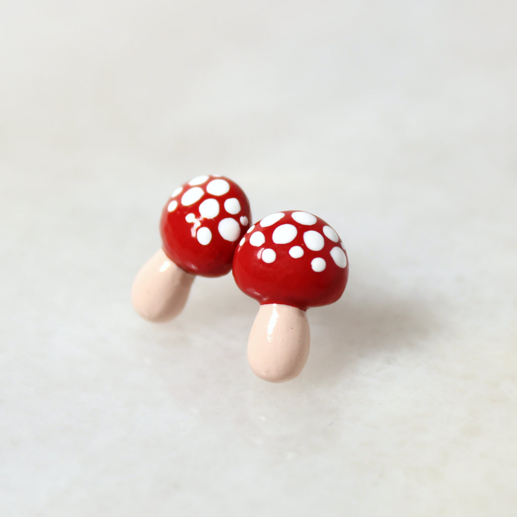 A pair of red mushroom earrings rest on top of a marble surface