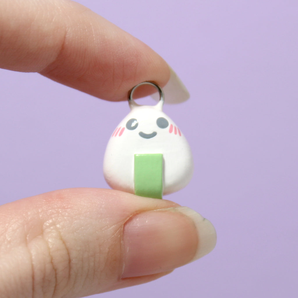 A hand holding an onigiri charm. The charm is about 3/4 of an inch tall.