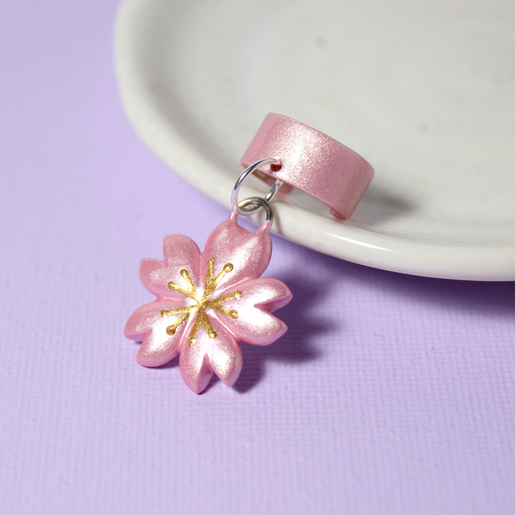A sparkly cherry blossom flower charm hangs off of a sparkly pink ear cuff