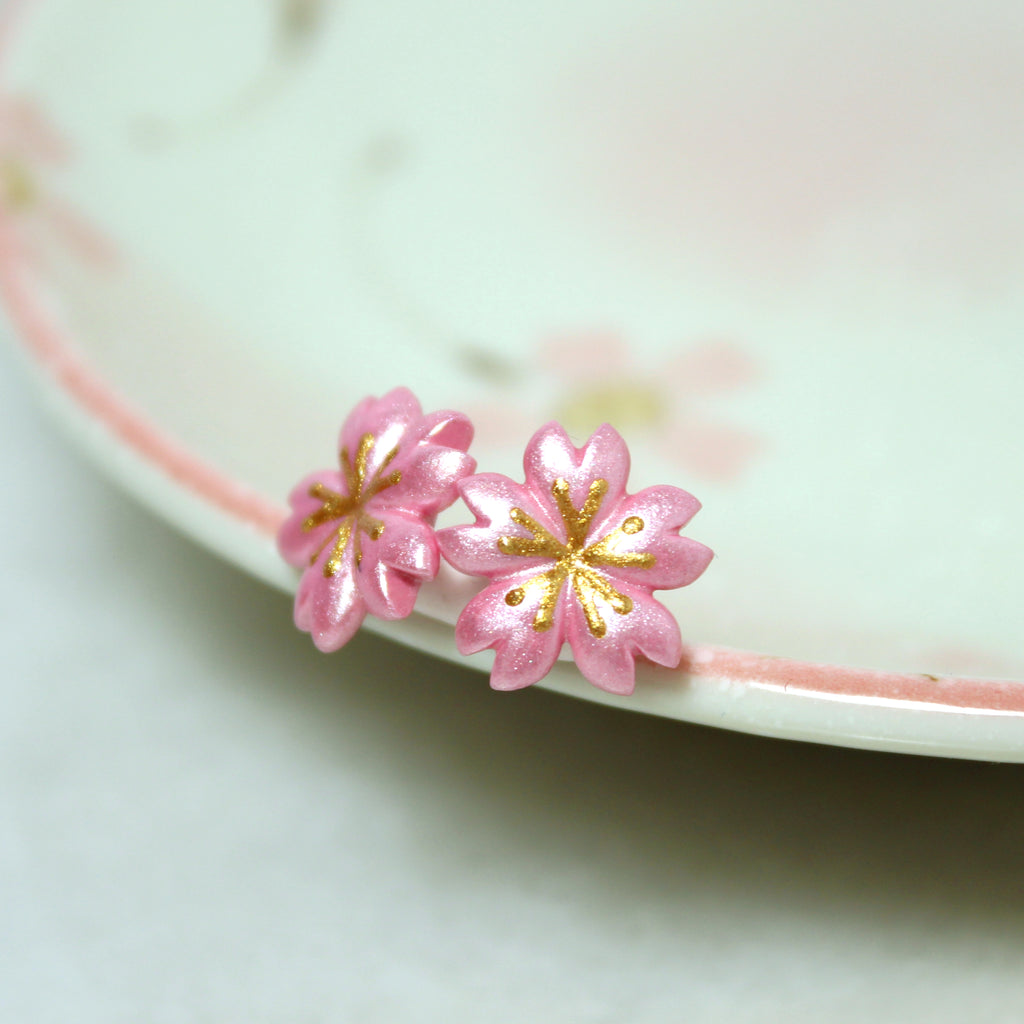 A pair of cherry blossom earrings rest against a jewelry dish.
