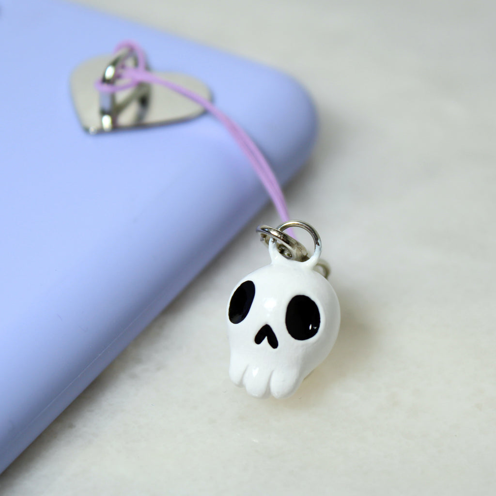 A miniature white and black skull phone charm hangs from a purple phone case