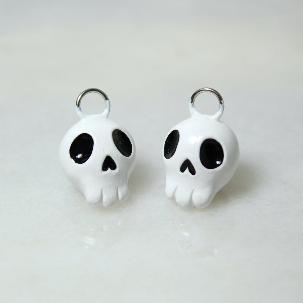 Two miniature skull charms sit next to each other on a marble surface