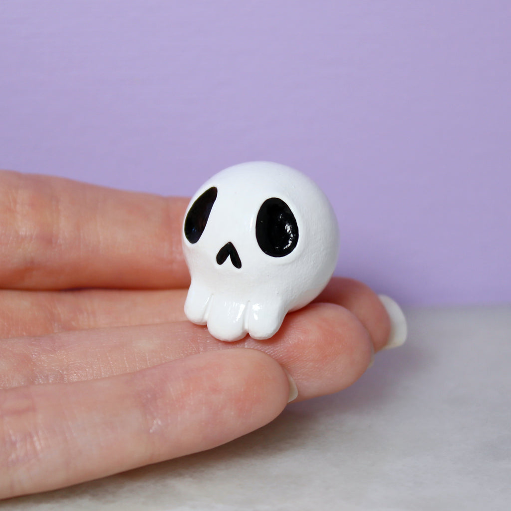A hand holds a miniature white skull figurine against a purple background