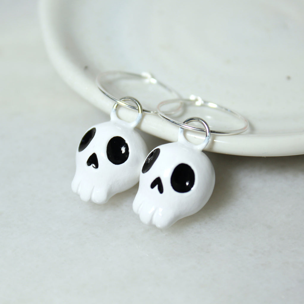 A pair of skull hoop earrings rest against a white jewelry dish