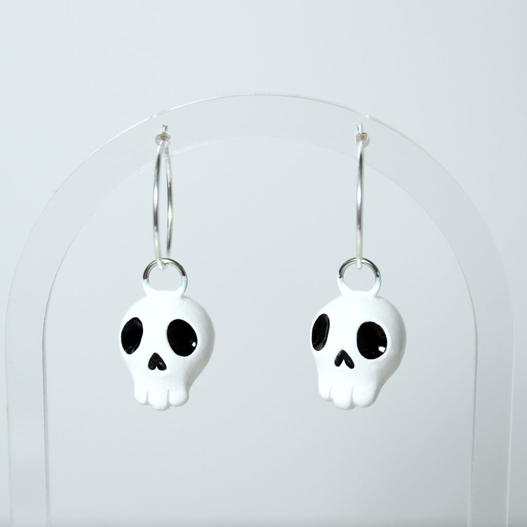 A pair of skull hoop earrings hang from a clear acrylic jewelry display