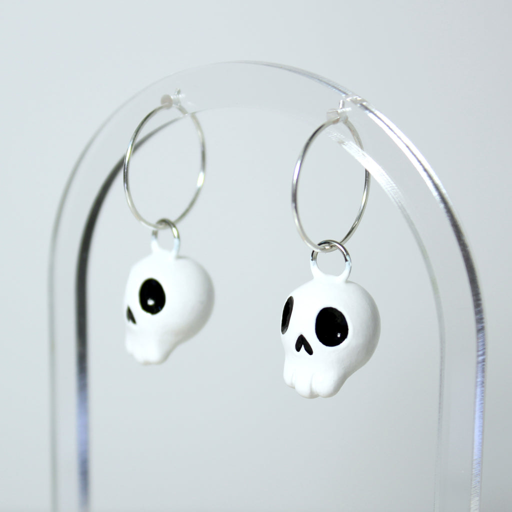 A pair of skull hoop earrings hang from a clear acrylic jewelry display