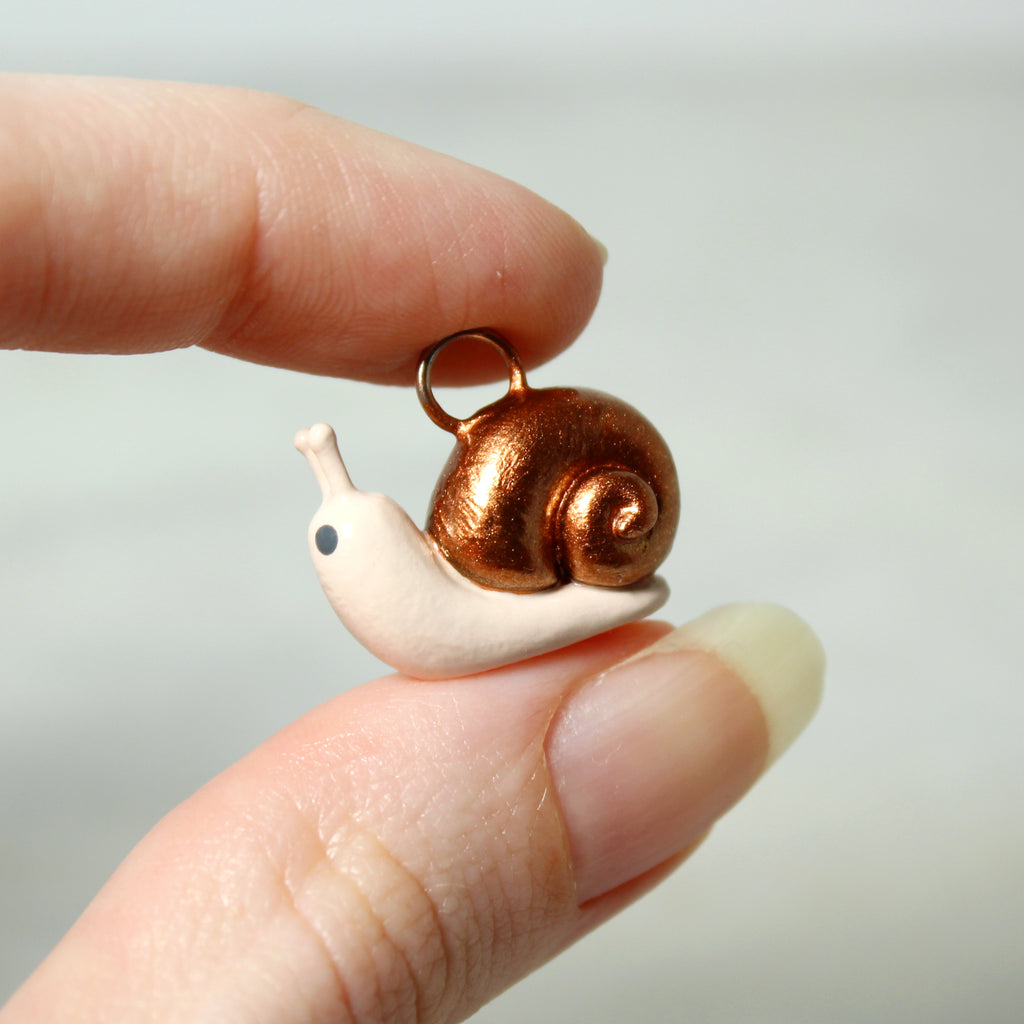 A hand holds a miniature snail charm with a sparkly bronze shell