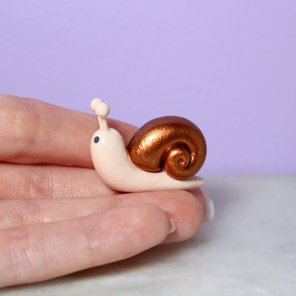 A hand holds a miniature snail figurine with a sparkly bronze shell
