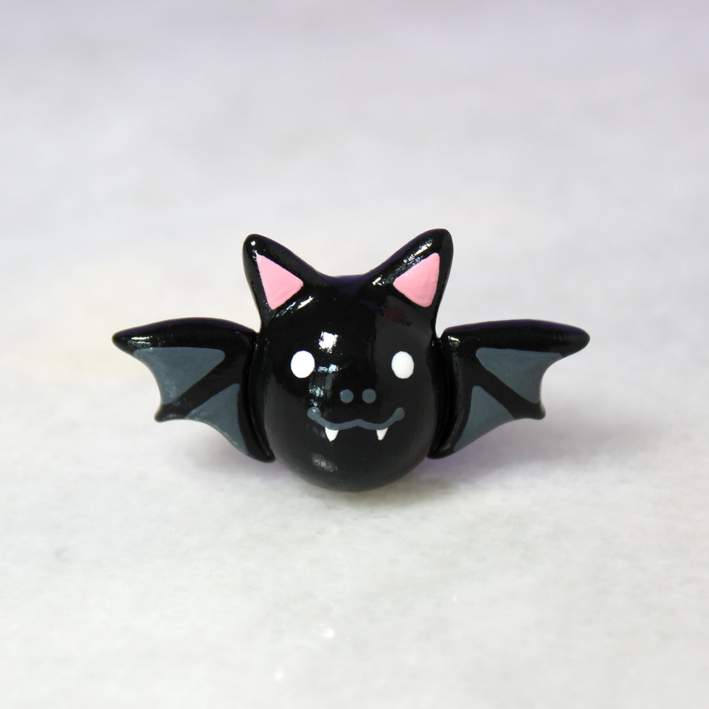 A small black bat figurine sitting on a shiny white surface.