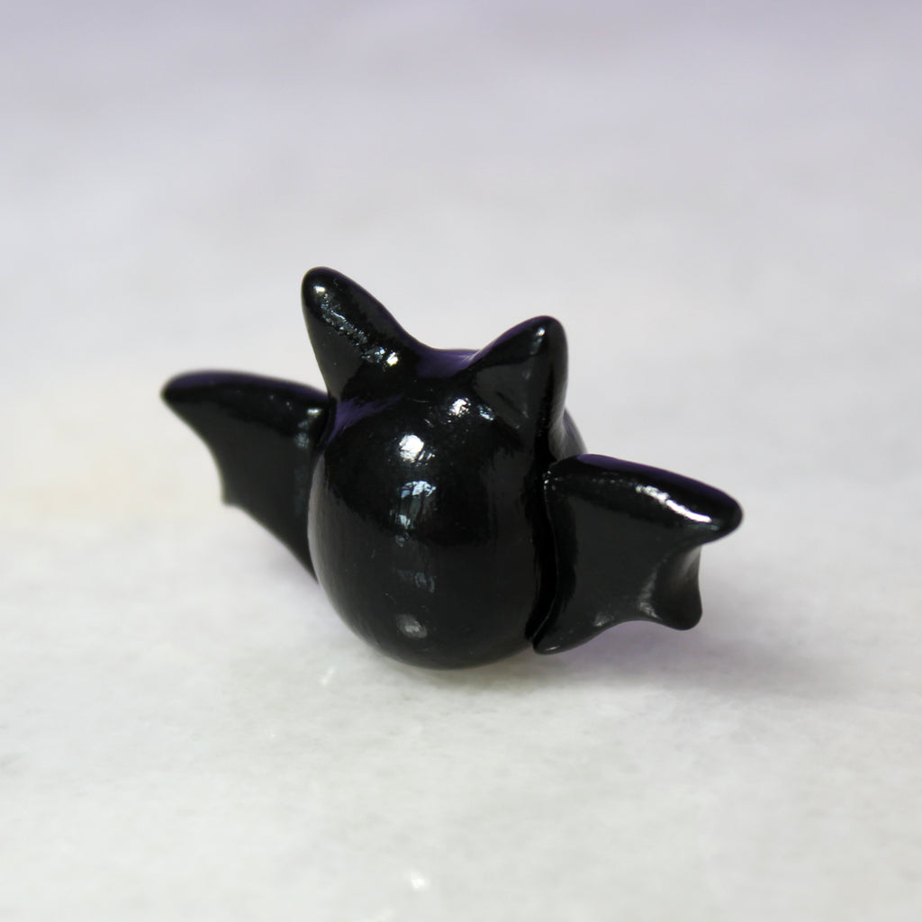 The backside of a small black bat figurine sitting on a shiny white surface.
