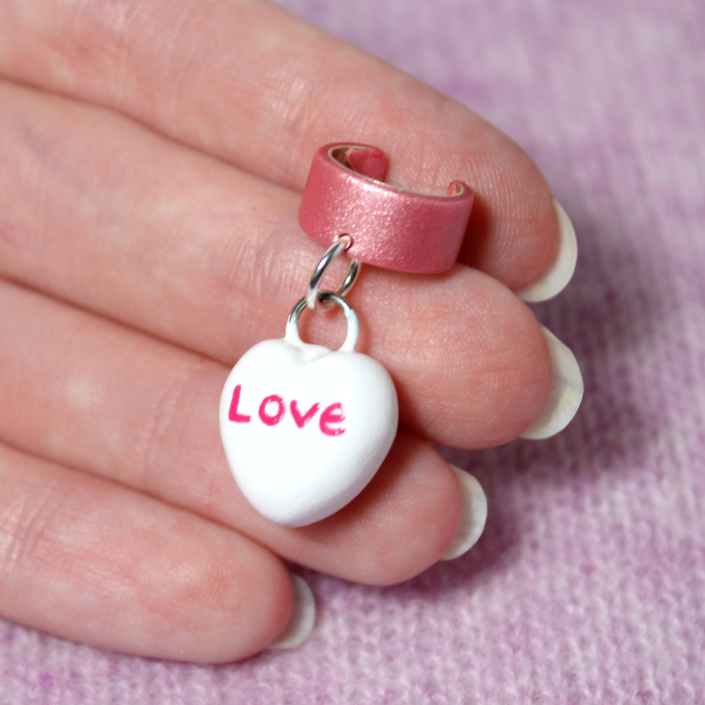 A hand holds a candy heart ear cuff. The candy heart charm is about 3/4 of an inch tall.