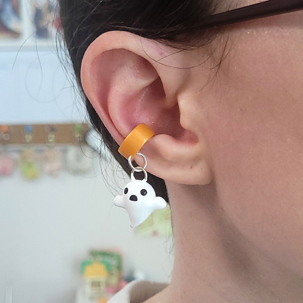 A ghost ear cuff hanging from an ear. The cuff wraps comfortably around the cartilage, and doesn't require any piercings.