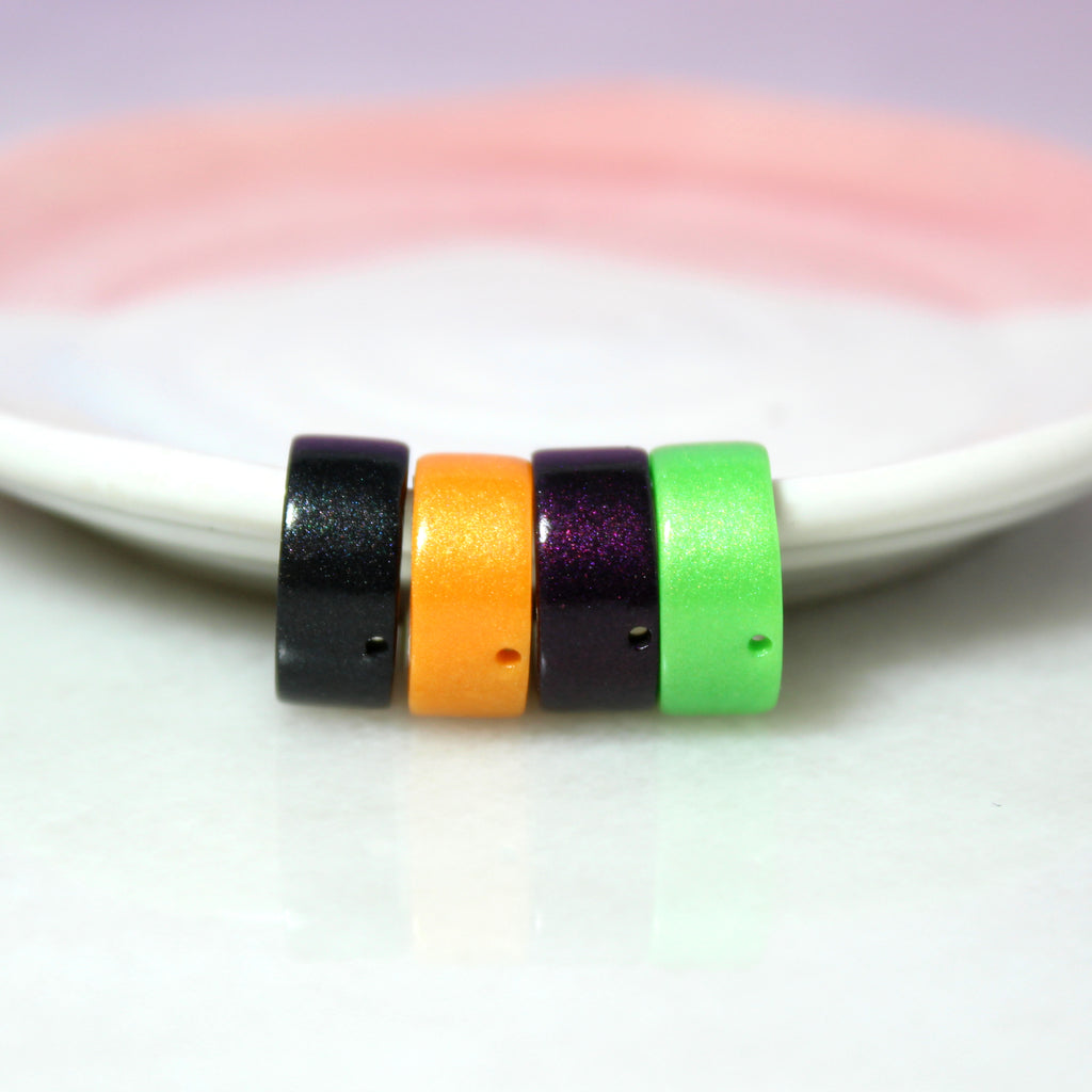 Four sparkly clay coated ear cuffs hang from a white and pink jewelry dish. From left to right there is a black cuff, a bright orange cuff, a dark purple cuff, and a bright green cuff.