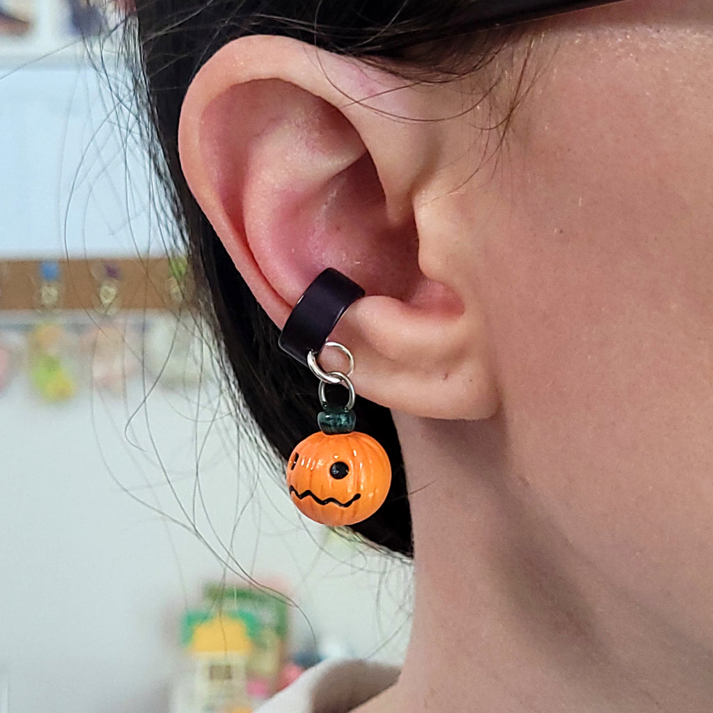 A jack o lantern ear cuff hangs from an ear. The cuff slides comfortably onto the cartilage and doesn't require any piercings to wear.