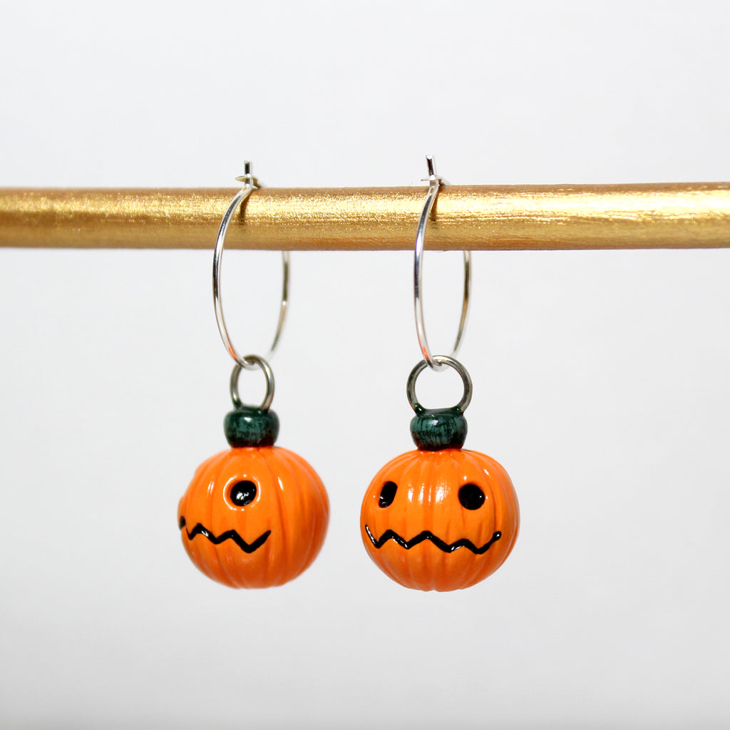 A pair of jack o lantern hoop earrings hang from a gold bar.