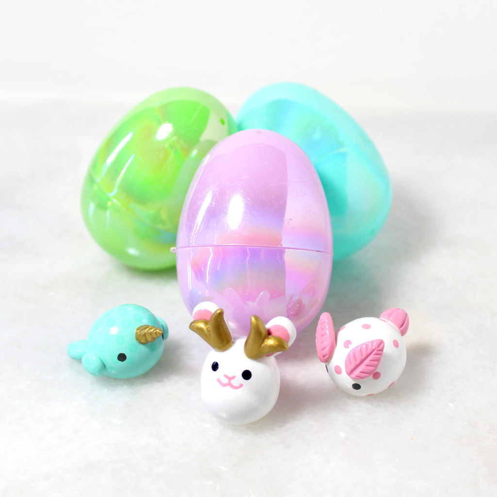 Three miniature figurines sit in front of three iridescent plastic easter eggs.