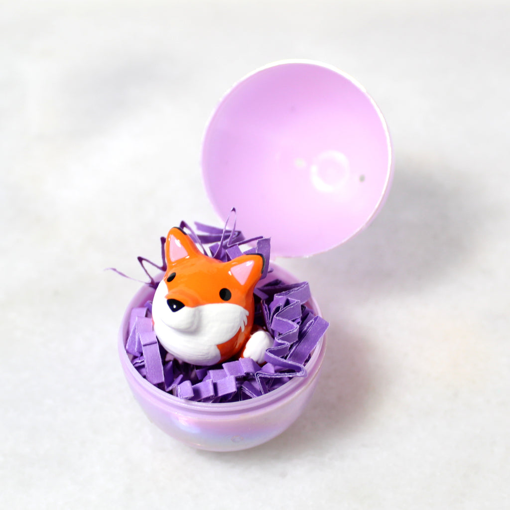 A miniature fox figurine sits in an opened plastic easter egg.