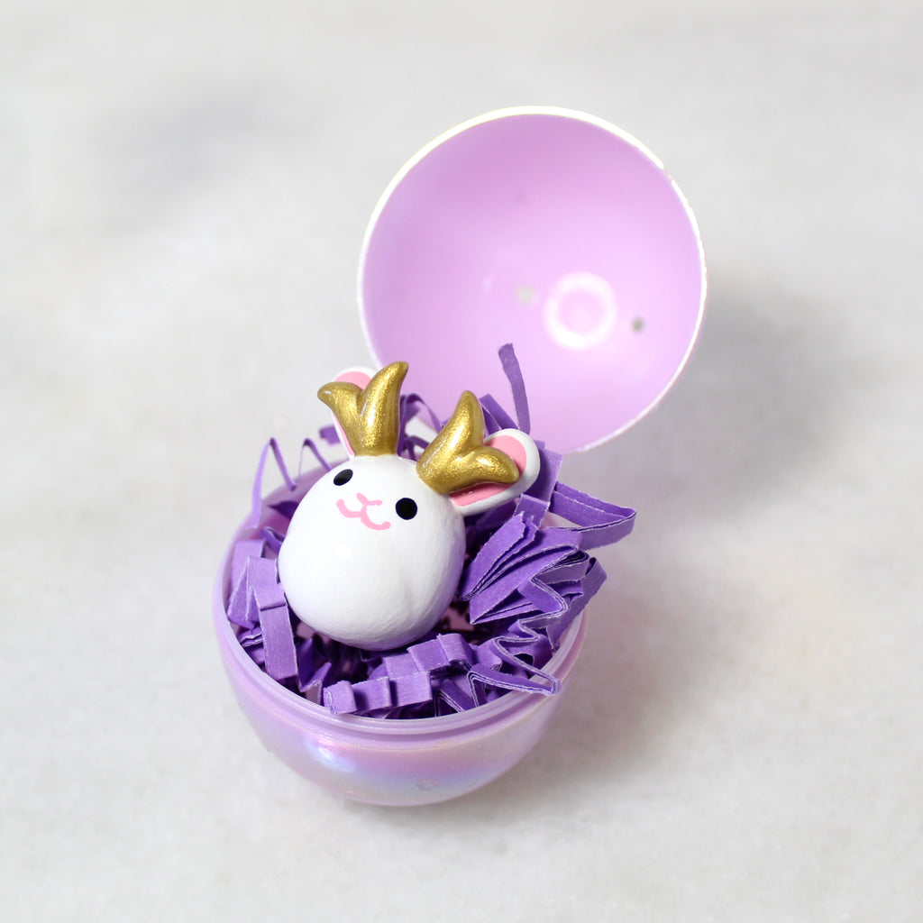 A miniature jackalope figurine sits in an opened plastic easter egg.