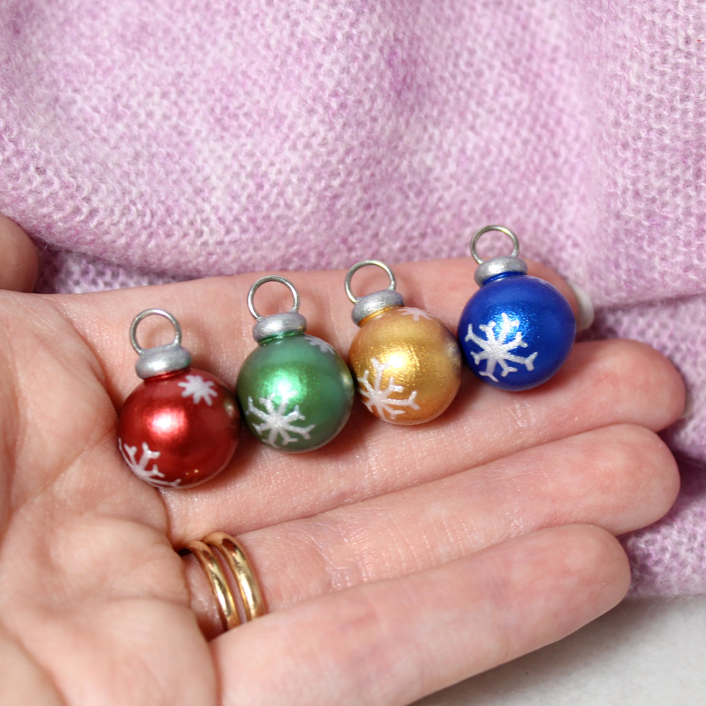 A hand holding four mini christmas ornament charms with sparkly snowflake designs.