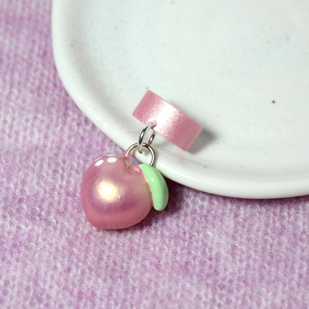 A pink gold peach charm hangs from a sparkly pink ear cuff.