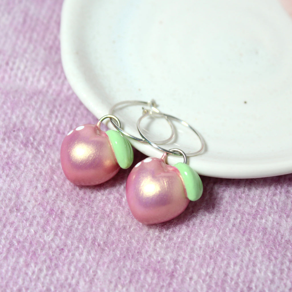 A pair of pastel metallic pink gold peach charms hang from sterling silver hoop earrings.