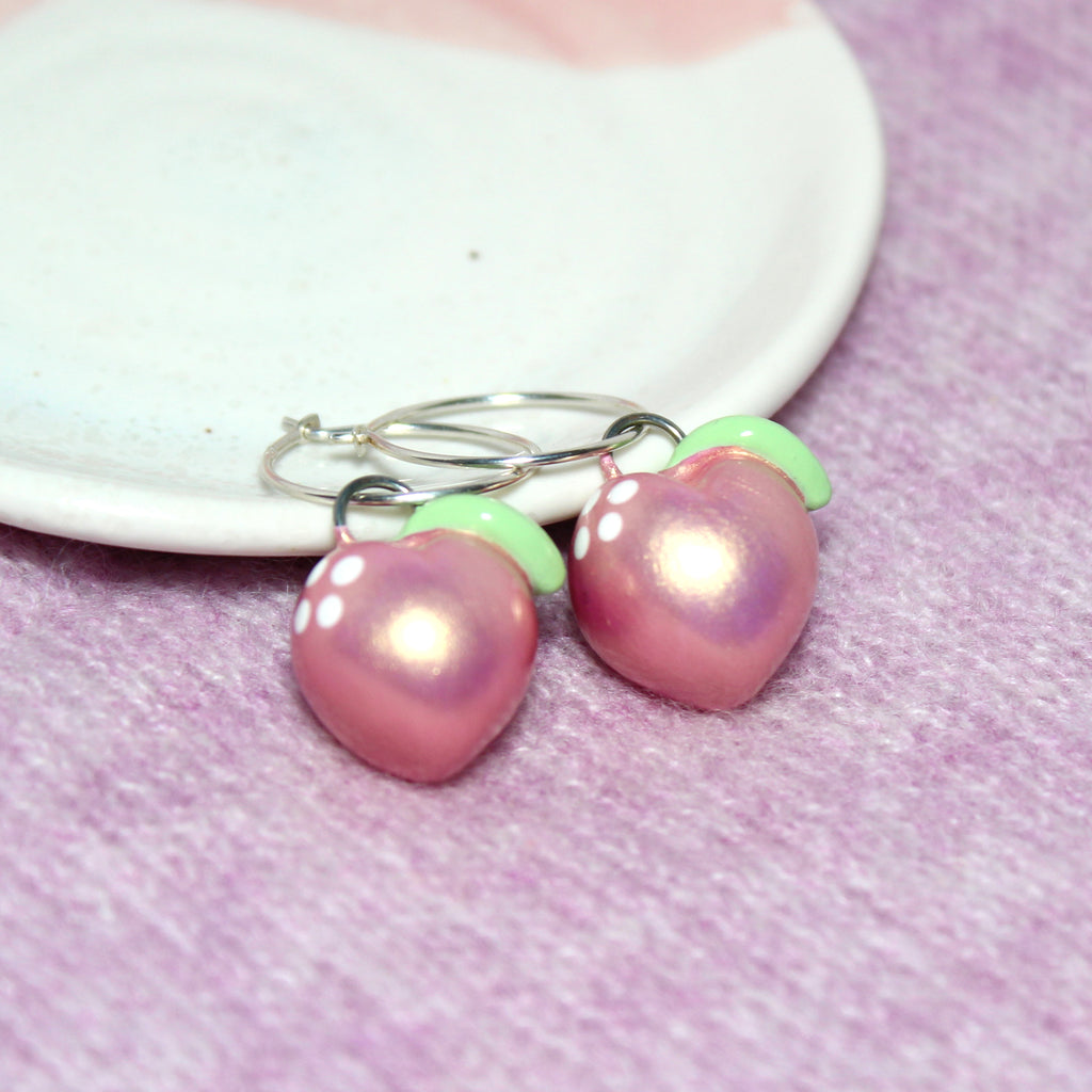 A pair of pastel metallic pink gold peach charms hang from sterling silver hoop earrings.