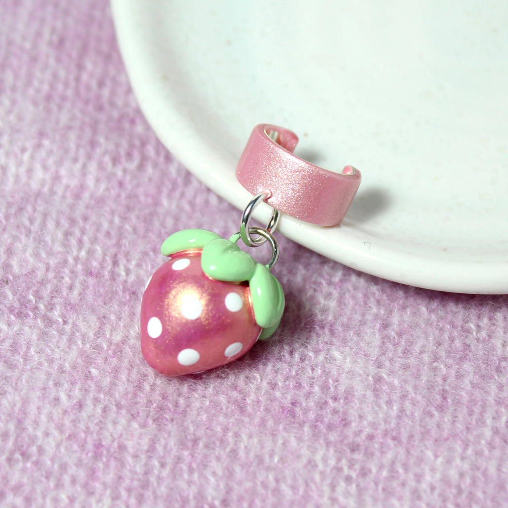 A pink gold strawberry charm hangs from a sparkly pink ear cuff.